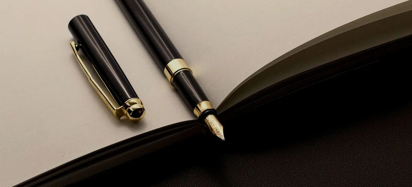 stylo plume noir et or posé sur un carnet ouvert, évoquant la construction soignée d'une identité de marque